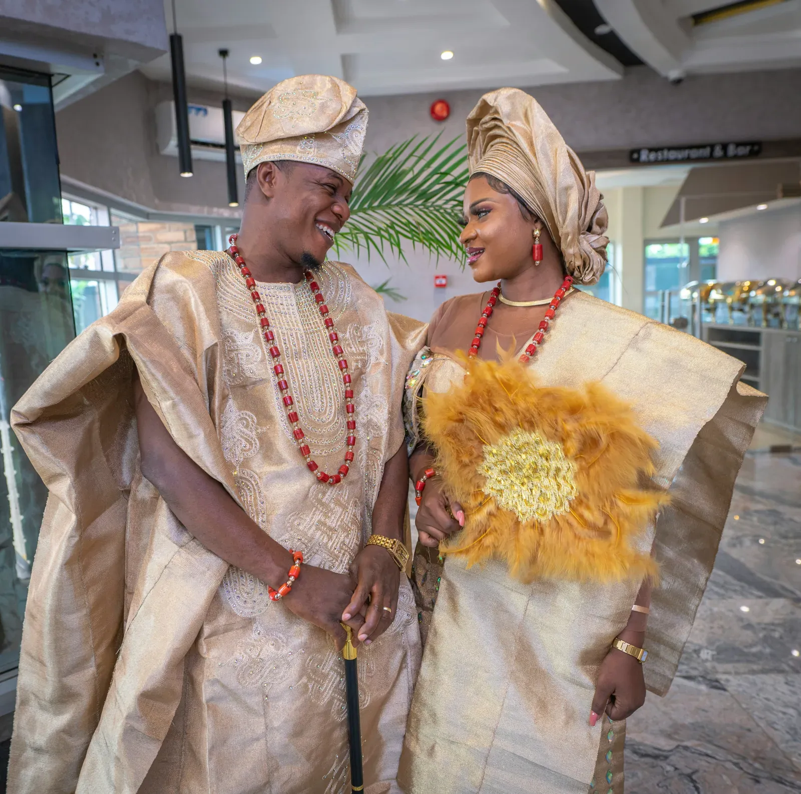 Brautpaar in passender goldfarbener Kleidung bei einer traditionellen Hochzeit in Nigeria, die Braut mit großem Gele-Kopftuch, der Bräutigam in weitem Gewand mit Kappe