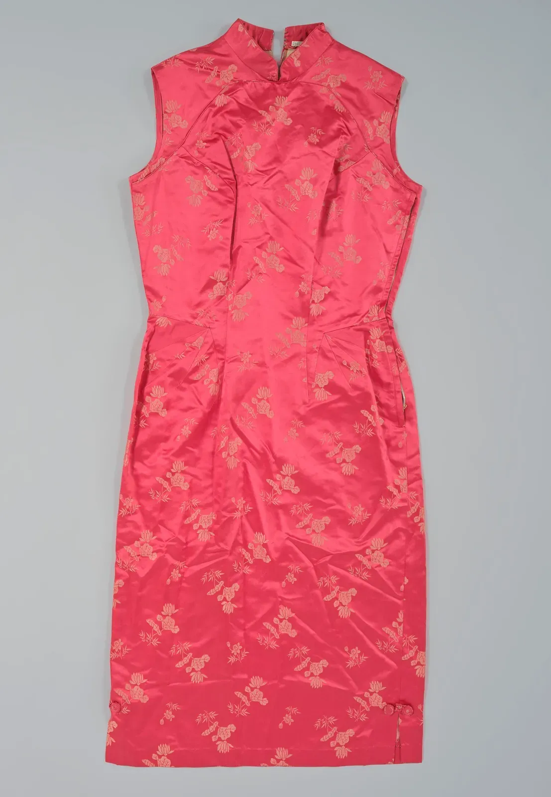 Tailliertes, ärmelloses korallenrotes Qipao mit hohem Stehkragen und kleinem eingewebtem Blumenmuster vor schlichtem grauem Hintergrund